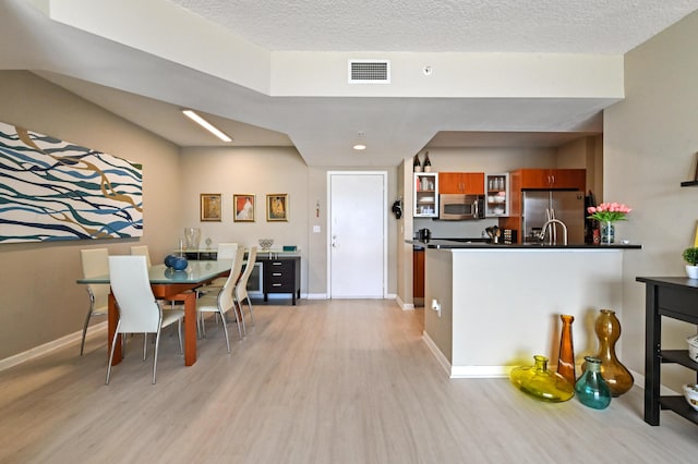 kitchen featuring dark countertops, visible vents, light wood-type flooring, brown cabinetry, and stainless steel appliances