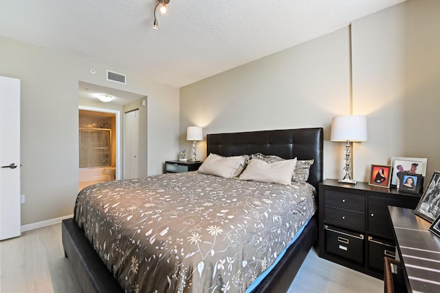 bedroom with wood finished floors, baseboards, visible vents, ensuite bathroom, and a textured ceiling