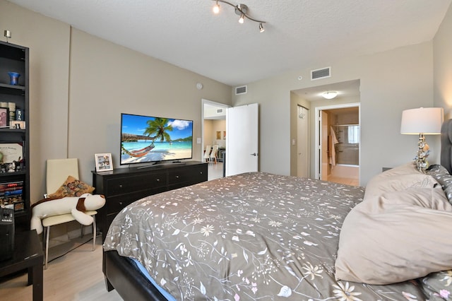 bedroom with visible vents, connected bathroom, a textured ceiling, and wood finished floors