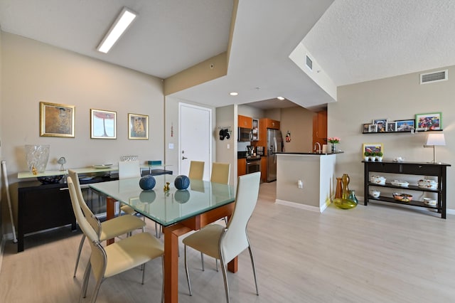 dining area featuring a textured ceiling, baseboards, visible vents, and light wood-type flooring