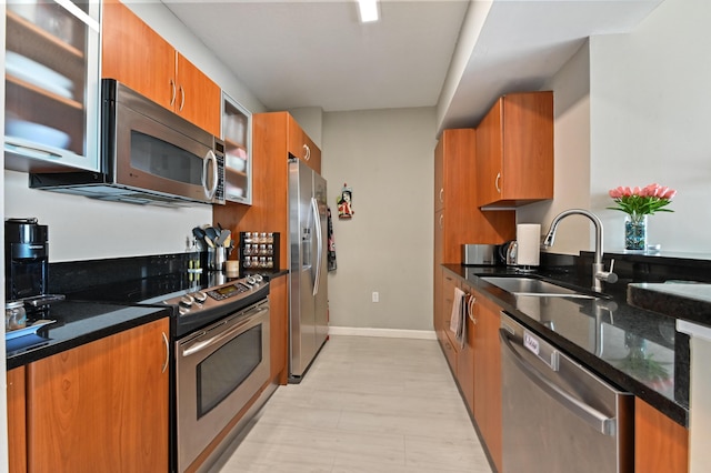 kitchen featuring baseboards, dark stone countertops, brown cabinets, stainless steel appliances, and a sink