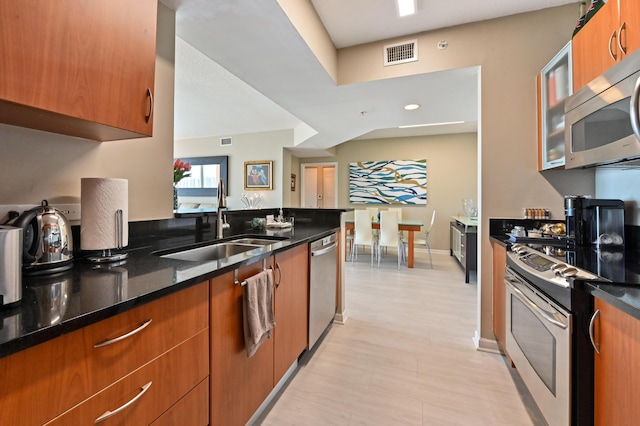 kitchen featuring visible vents, brown cabinets, a sink, stainless steel appliances, and dark stone counters