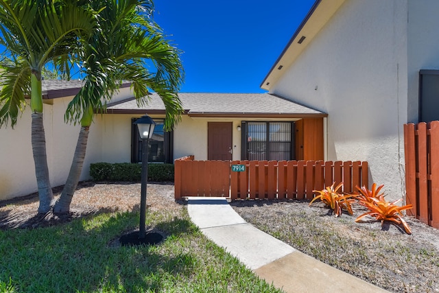 view of front of property featuring stucco siding, roof with shingles, and a fenced front yard