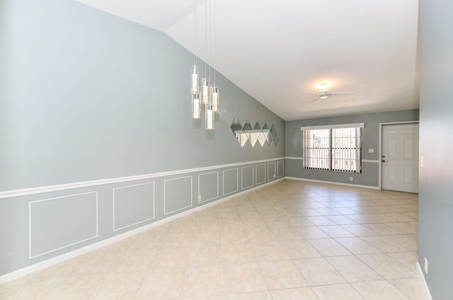 empty room with vaulted ceiling, a decorative wall, light tile patterned floors, and a wainscoted wall