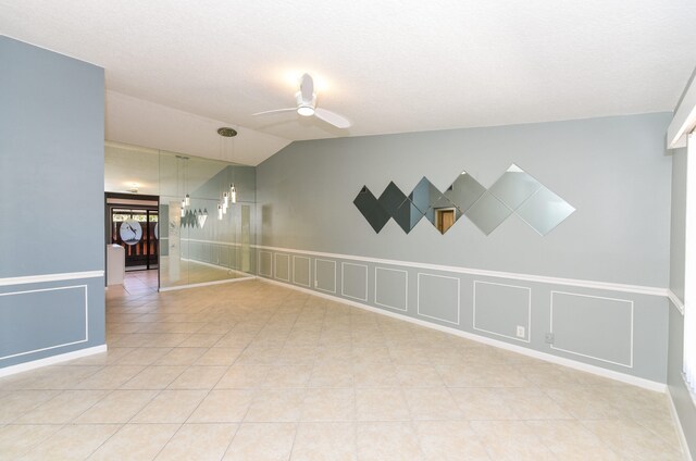 empty room featuring light tile patterned floors, ceiling fan, vaulted ceiling, and a decorative wall