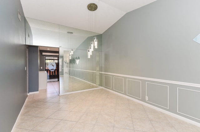 empty room with lofted ceiling, a decorative wall, light tile patterned flooring, and a wainscoted wall