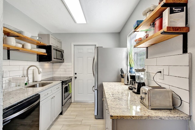 kitchen with light stone countertops, open shelves, a sink, decorative backsplash, and appliances with stainless steel finishes