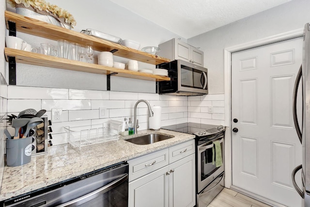 kitchen with open shelves, light stone countertops, decorative backsplash, appliances with stainless steel finishes, and a sink