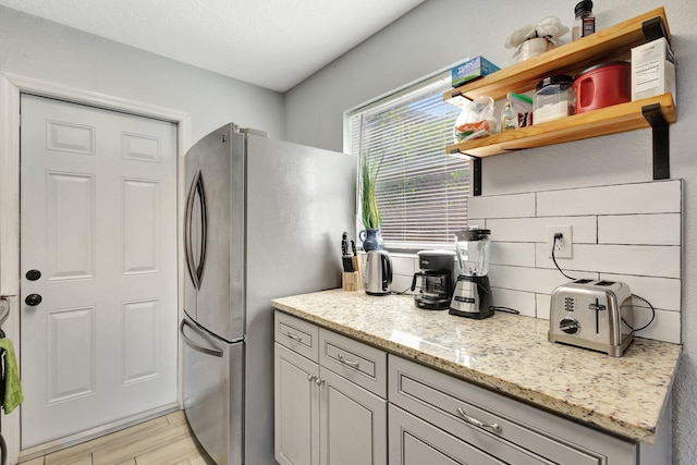 kitchen with light stone countertops, freestanding refrigerator, light wood-style floors, and open shelves