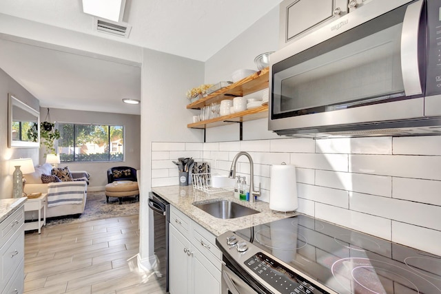 kitchen with visible vents, a sink, appliances with stainless steel finishes, decorative backsplash, and light stone countertops