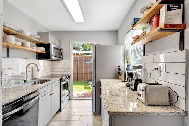 kitchen with light stone countertops, open shelves, a sink, stainless steel appliances, and tasteful backsplash