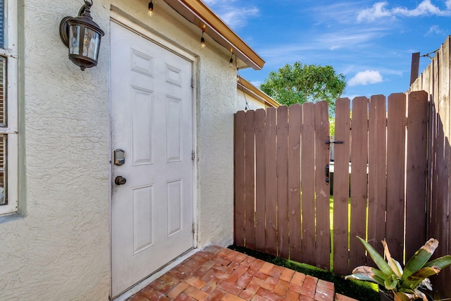 view of exterior entry featuring a gate, stucco siding, and fence