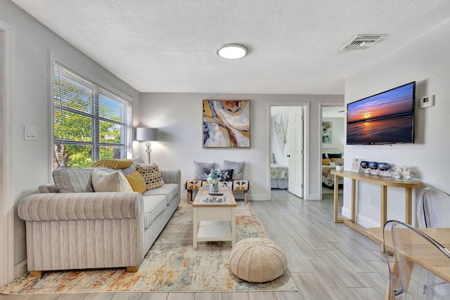 living area featuring visible vents, a textured ceiling, baseboards, and wood tiled floor