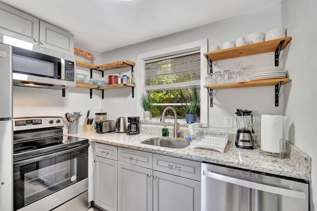 kitchen with open shelves, light stone counters, appliances with stainless steel finishes, and a sink