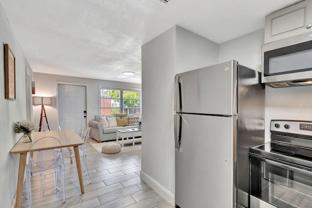 kitchen with baseboards, wood tiled floor, appliances with stainless steel finishes, a textured ceiling, and open floor plan