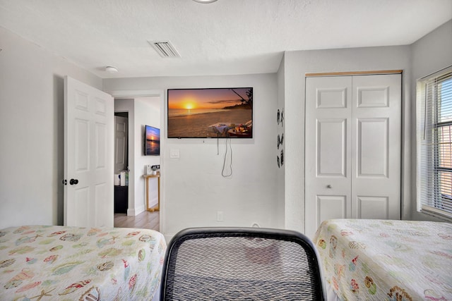 bedroom with light wood-style floors, visible vents, a closet, and a textured ceiling