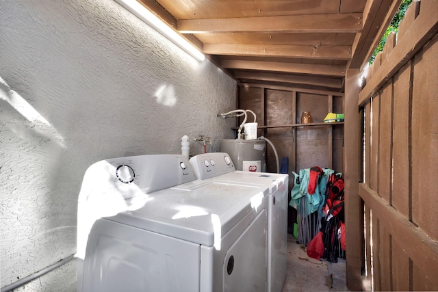 clothes washing area featuring water heater, separate washer and dryer, laundry area, and a textured wall