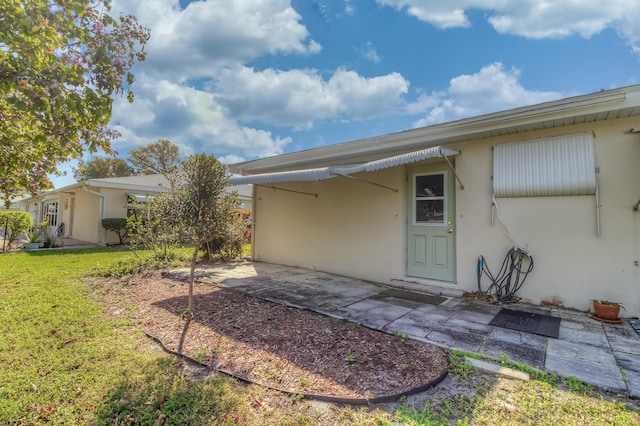 entrance to property with a patio, a lawn, and stucco siding