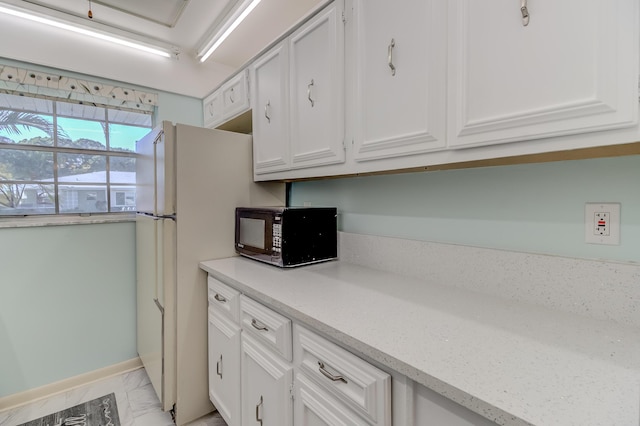 kitchen with baseboards, marble finish floor, black microwave, and white cabinetry