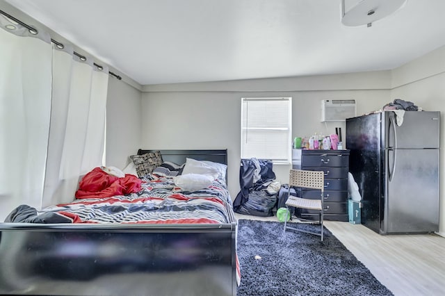 bedroom featuring a wall mounted air conditioner, wood finished floors, and freestanding refrigerator