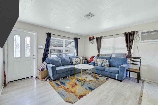 living area featuring visible vents, plenty of natural light, an AC wall unit, and light wood-type flooring