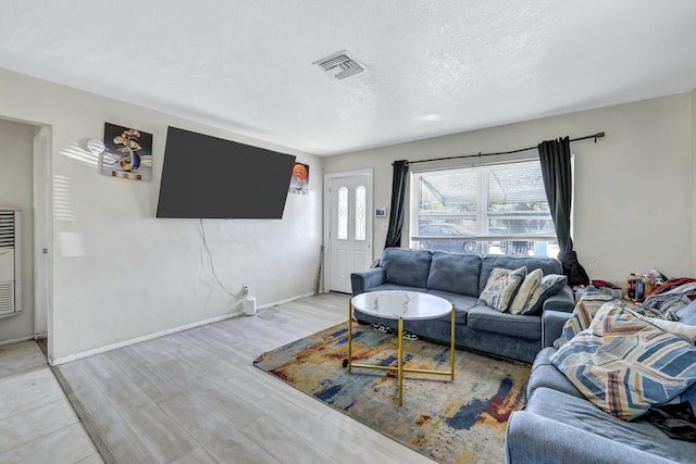 living room with light wood finished floors, visible vents, a textured ceiling, and baseboards