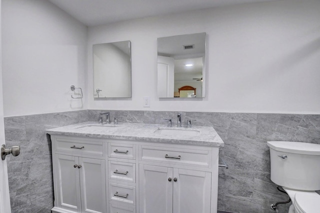 bathroom featuring tile walls, toilet, visible vents, and a sink