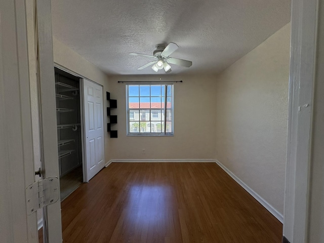 unfurnished bedroom with a textured ceiling, dark wood-style floors, a closet, baseboards, and ceiling fan