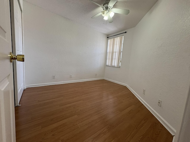 empty room with dark wood-type flooring, a ceiling fan, baseboards, and a textured wall