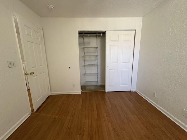 unfurnished bedroom with a textured wall, wood finished floors, baseboards, and a closet