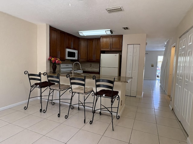 kitchen with visible vents, white appliances, a breakfast bar area, and a peninsula