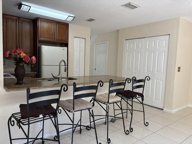 kitchen featuring a breakfast bar area, visible vents, freestanding refrigerator, a sink, and a textured ceiling