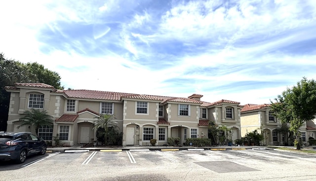 view of front facade featuring stucco siding, a tile roof, and uncovered parking