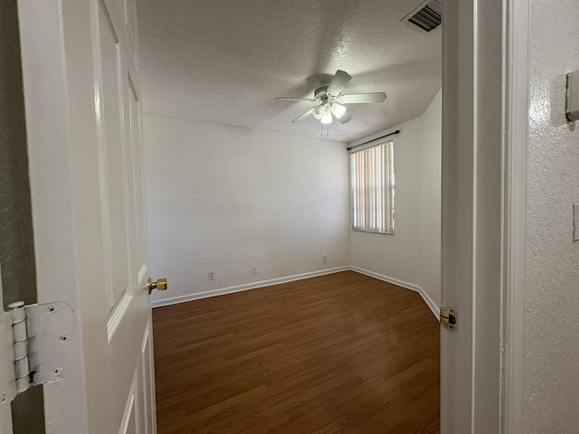 empty room featuring a ceiling fan, baseboards, visible vents, dark wood-style flooring, and a textured ceiling