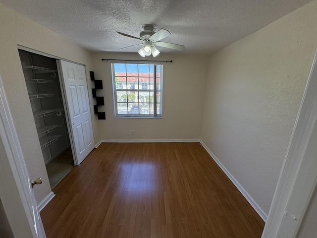 interior space featuring a textured ceiling, baseboards, dark wood-type flooring, and ceiling fan