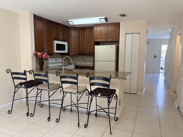 kitchen with visible vents, a kitchen bar, light tile patterned floors, a peninsula, and white appliances