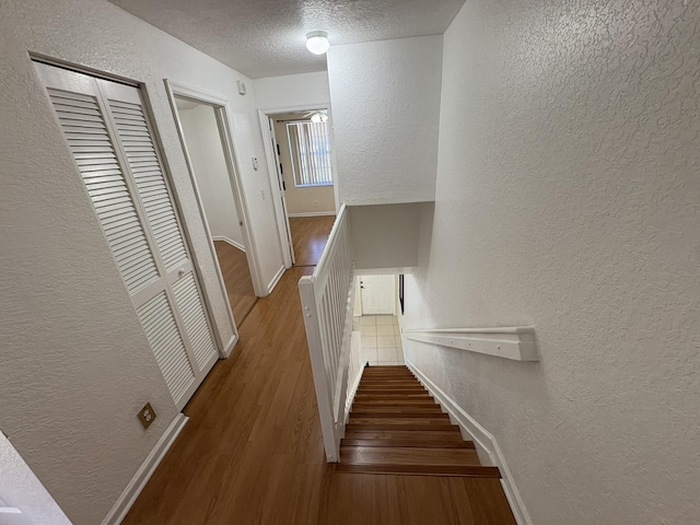 stairway with wood finished floors, a textured wall, baseboards, and a textured ceiling