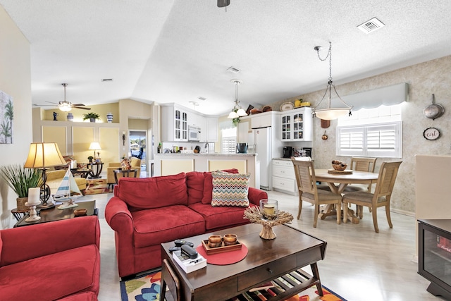 living room featuring wallpapered walls, visible vents, plenty of natural light, and vaulted ceiling