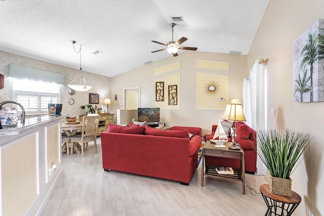 living area with visible vents, a textured ceiling, lofted ceiling, and light wood-style floors