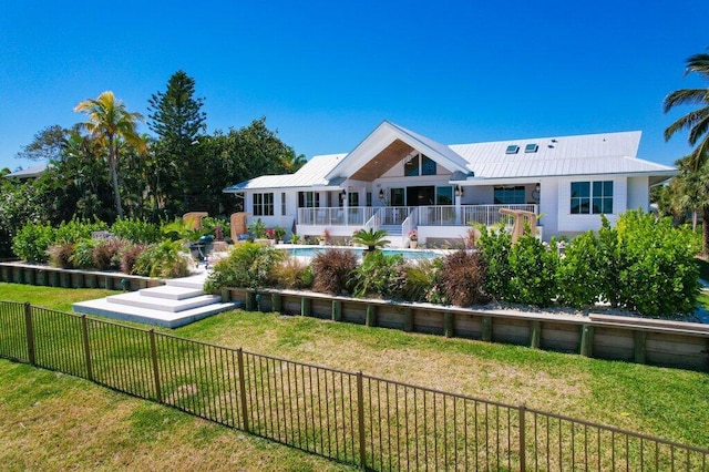 rear view of property with a yard, a fenced in pool, a fenced backyard, and metal roof