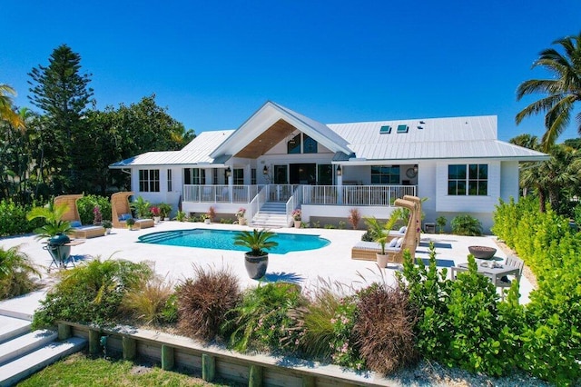 rear view of property with a patio, a wooden deck, an outdoor pool, stairs, and metal roof