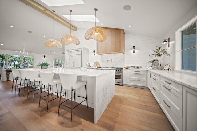 kitchen with backsplash, light wood-style flooring, a skylight, and high end stainless steel range