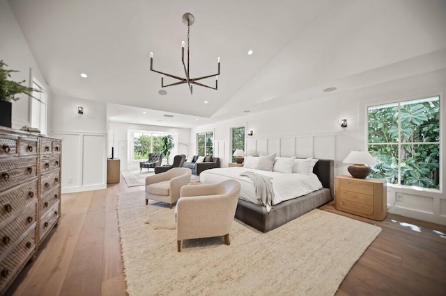 bedroom with a wainscoted wall, high vaulted ceiling, light wood-style floors, a decorative wall, and a notable chandelier