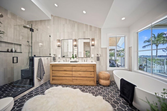 bathroom with a soaking tub, double vanity, lofted ceiling, a stall shower, and tile walls