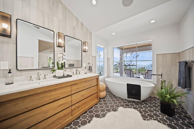 bathroom with double vanity, a freestanding bath, tile walls, and a sink