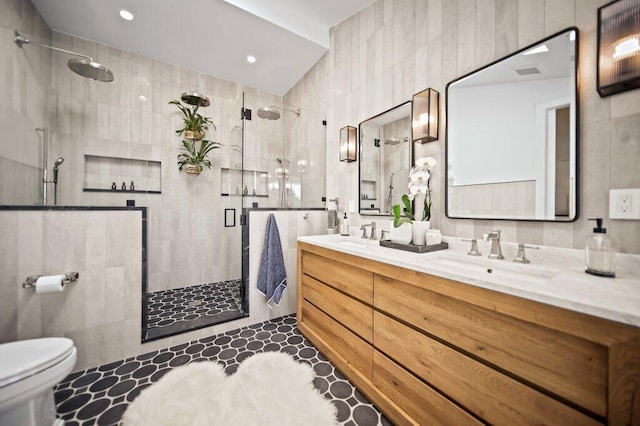 full bath with a shower stall, toilet, double vanity, tile walls, and a sink