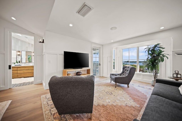 living room featuring visible vents, light wood finished floors, lofted ceiling, recessed lighting, and a decorative wall