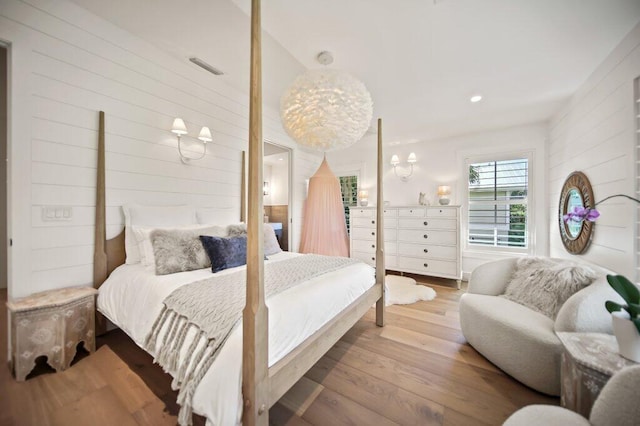 bedroom with wooden walls, wood finished floors, and visible vents