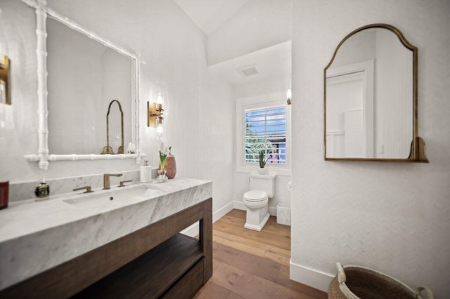 bathroom with baseboards, toilet, vaulted ceiling, wood finished floors, and vanity