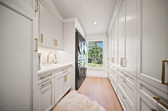 laundry room with light wood finished floors, recessed lighting, cabinet space, a sink, and stacked washer / dryer